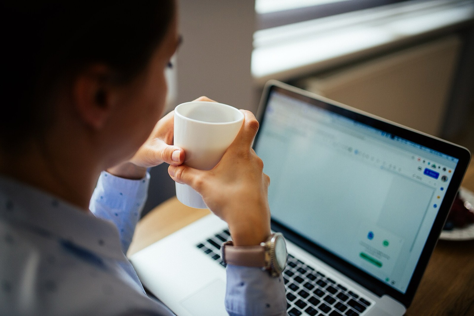 Iemand met een kop koffie kijkt op een laptop.