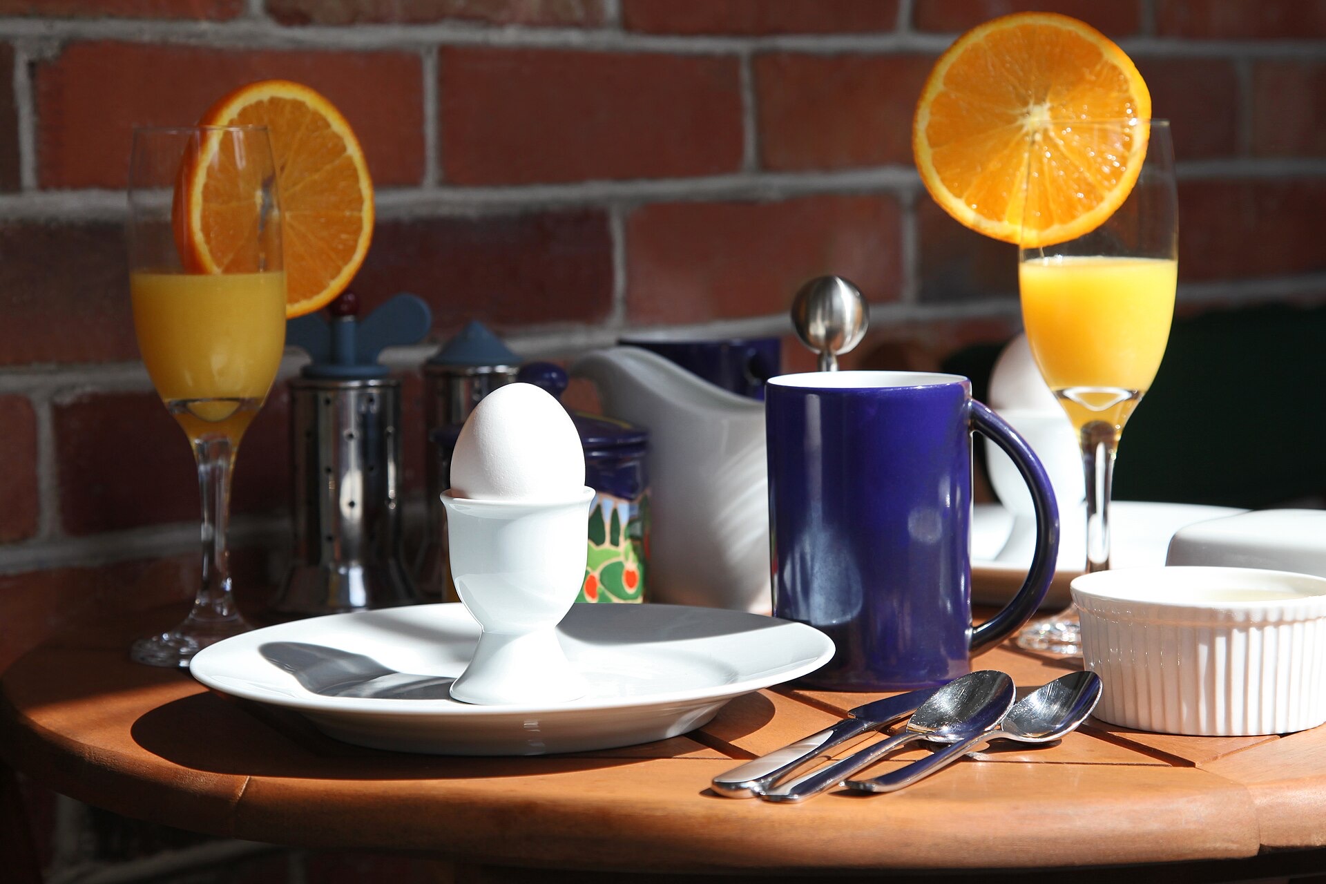 Ontbijttafel in de ochtendzon met een kobaltblauwe mok, een eitje en twee glazen sinaasappelsap.